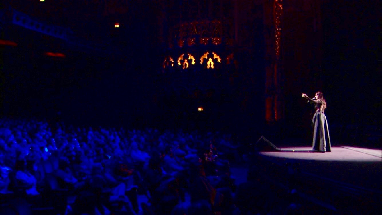 Lucinda Belle alone on a vast arena stage, spotlit before a full house